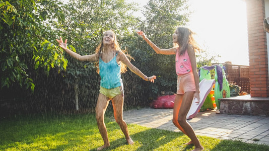 家庭在夏季户外玩耍和乐照片来自两个穿着湿衣服的欢笑姐妹在花园的水龙头滴下跳舞图片