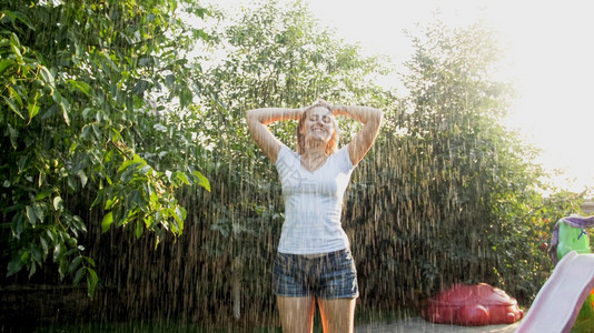 穿着湿衣服的美丽微笑女子肖像在日落时家庭后院花园享受雨女孩在夏季户外玩耍和乐穿着湿衣服的美丽微笑女子肖像在日落时家庭后院花园享受图片