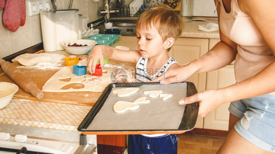 3岁幼儿男孩与母亲一起做饼干的近身肖像Child拿着烤锅并在上面贴饼干可爱3岁幼儿男孩与母亲一起做饼干的近身肖像图片