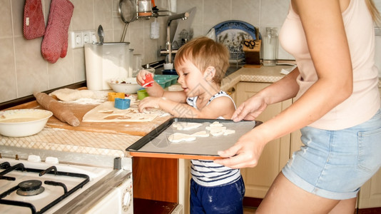 3岁幼儿男孩与母亲一起做饼干的近身肖像Child拿着烤锅并在上面贴饼干可爱3岁幼儿男孩与母亲一起做饼干的近身肖像图片