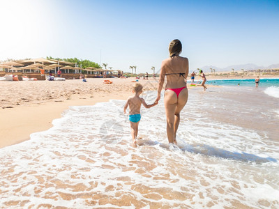 快乐的年轻母亲与孩子的儿一起在美丽的海边散步照片家庭在暑假期间放松和享受愉快的时光乐年轻母亲与孩子的儿一起在美丽的海边散步图像家图片