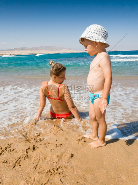 小男孩和母亲在沙滩上放松温暖的海洋波浪中放松家庭暑假期间玩得愉快小男孩和母亲在温暖的海洋波浪中沙滩上放松家庭暑假期间过得很愉快图片
