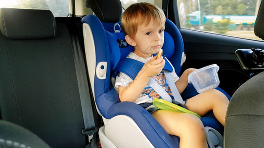 坐在汽车儿童安全座椅上吃饼干的男孩肖像图片