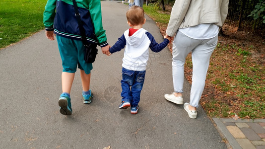 欢乐家庭与幼儿男孩握着手在公园中行走的照片图片