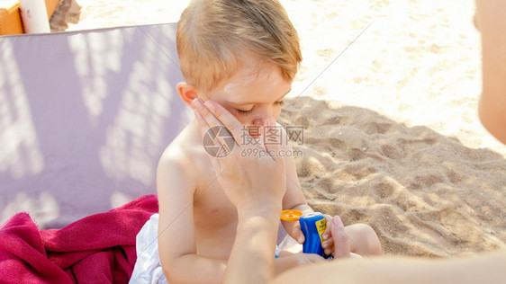 与年轻母亲一起坐在海边的太阳床并涂防晒油的可爱幼儿男孩肖像与年轻母亲一起坐在沙滩的阳光床上并涂防晒油的可爱幼儿男孩肖像与年轻母亲图片