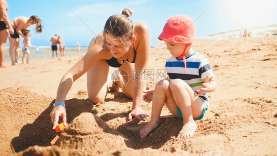 母亲教她孩子在海边用沙建造城堡家庭图片