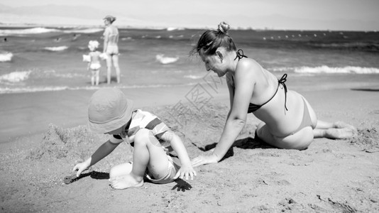 母亲与儿子一起坐在海边建造沙堡的黑白照片图片