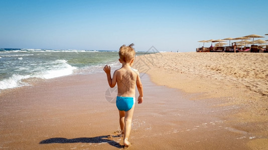 3岁幼儿男孩在湿海滨沙滩上行走的照片图片