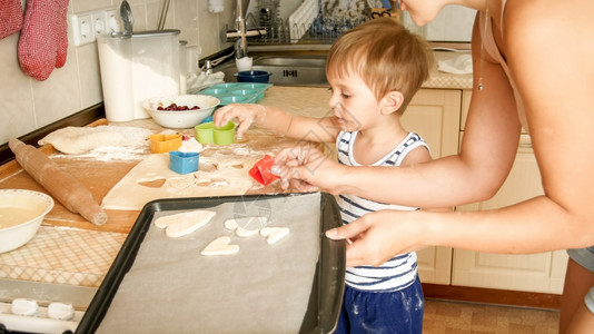 母亲与幼儿男孩的近亲肖像他们握着烘烤锅和厨房做饼干图片