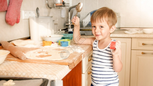 3岁男孩在烹饪和闭着看时拿大勺子在厨房里做饭时用着大勺子在厨房里做饭时用着大勺子在厨房里做饭和闭着看时用大勺子的笑3岁男孩的肖像背景图片