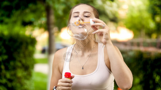 快乐的微笑女人肖像在夏日公园吹着彩色肥皂泡沫快乐的微笑年轻女人肖像在夏日公园吹着彩色肥皂泡沫图片