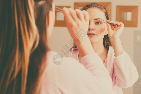 女人用tweezers挖眉毛吸引人的女孩用tweezes的眼睛眉看浴室的镜子图片