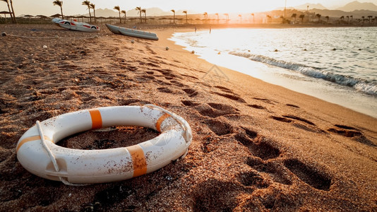 紧贴近距离的照片拯救生命的戒指躺在海刺砂上美丽的日落在海洋上紧贴的拯救生命戒指图像躺在海刺沙上图片