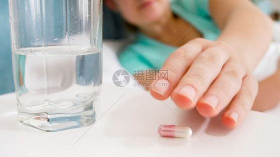 病态妇女到床边桌去取药片和水杯的近距离图像病态妇女到床边桌去取药片和水杯的近距离图像图片