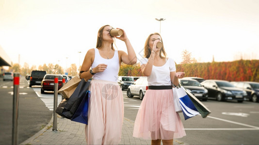 两个美丽的年轻女孩拿着购物袋用纸杯咖啡喝图片