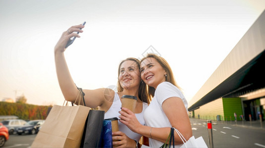 在商场购物后两个女朋友在商场购物后制作自拍智能手机照片的肖像图片