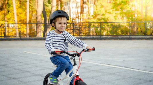 戴着防护头盔的可爱男孩在公共园骑自行车图片
