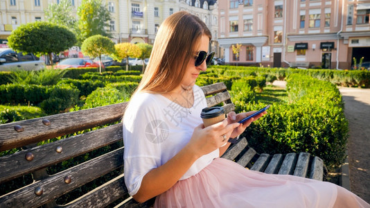 使用智能手机和喝咖啡的公园中美丽年轻女子图片