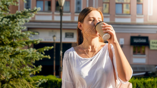 美丽时髦女孩在街上散步时喝纸杯咖啡因的肖像图片