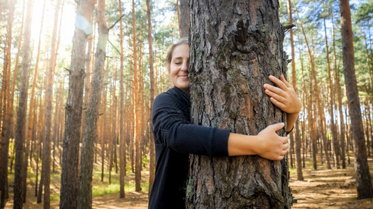 美丽笑容的年轻女子肖像在森林中倾斜和拥抱大树爱生态保护和与自然谐相处的概念图片