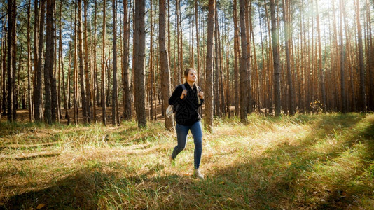 美丽的女远足者背着包走出草地上的森林美丽女远足者背着包走出森林的草地上图片