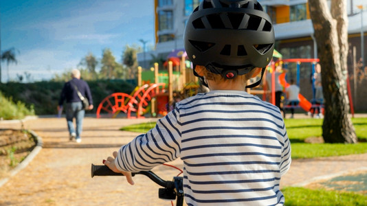 在公园骑自行车的小男孩头上戴黑色保护盔的照片图片