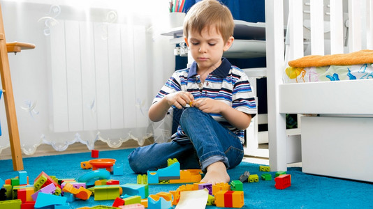 与玩具块在地毯上相邻的小集中男孩肖像与玩具块在地毯上相交的小集中男孩肖像图片