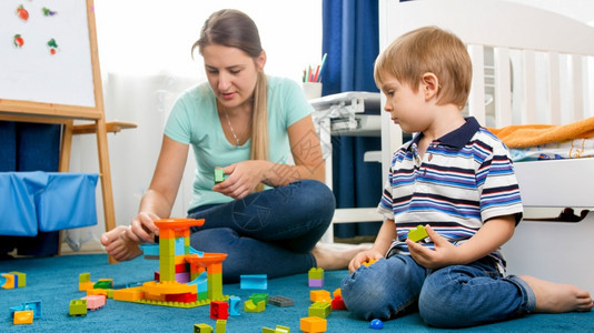 年轻母亲帮助她的儿子在游戏室地毯上组装玩具制造器图片