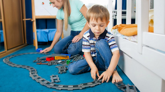 可爱的小男孩和他年轻母亲在卧室的地板上玩具铁路图片