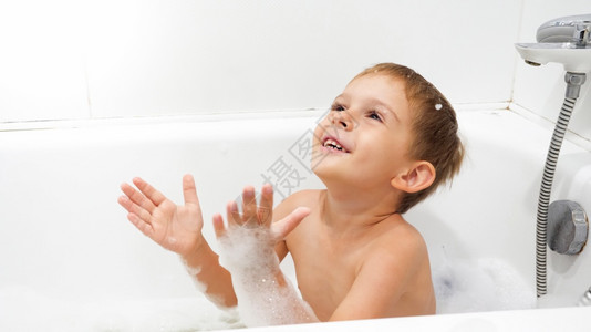 快乐笑的小男孩在洗澡时享受用肥皂泡沫洗浴的肖像图片