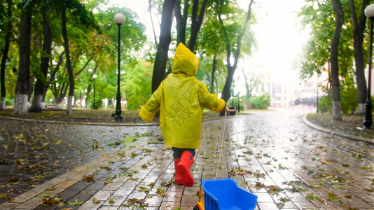 雨天在公园穿雨衣拿绳子拖玩具卡车的男孩图片