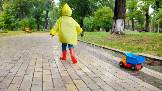 雨天在公园穿雨衣拿绳子拖玩具卡车的男孩图片
