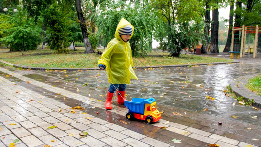 雨天在公园穿雨衣拿绳子拖玩具卡车的男孩图片