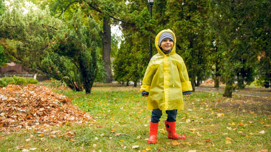 快乐的男孩在公园下雨后穿着黄色衣和红橡皮靴图片