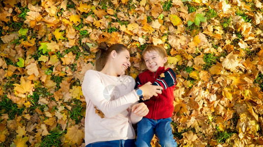 带着年轻母亲躺在秋天公园的树叶上图片