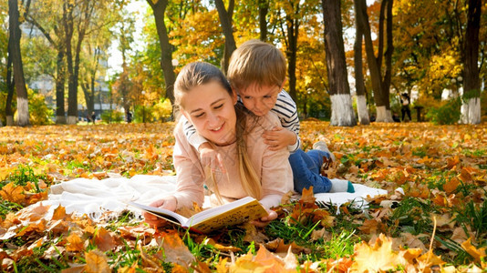 可爱的小孩男坐在母亲背上秋季公园读一本书图片