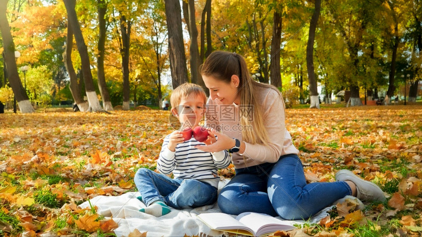 母亲和儿子在秋天公园毯子上野餐图片