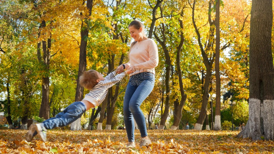 年轻母亲用手抱着儿子在秋天公园翻转儿子图片
