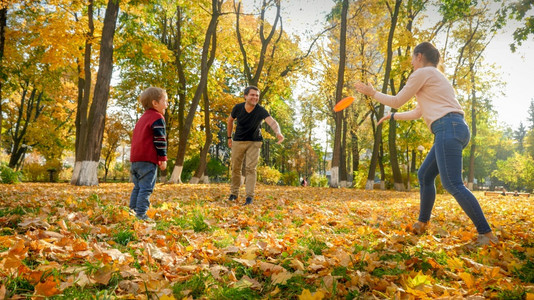 快乐的年轻父母在秋天公园的飞盘上与儿子玩耍图片