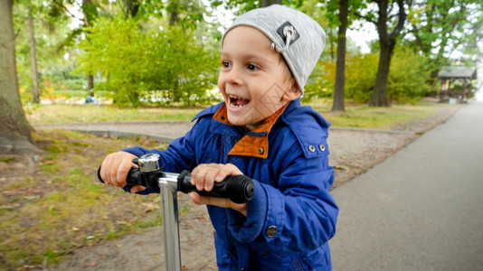 笑着的小男孩在公园骑着脚踏车时手持方向盘脚踏摩托车图片