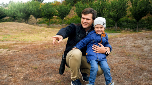 快乐的父亲拥抱他儿子用手指着公园图片