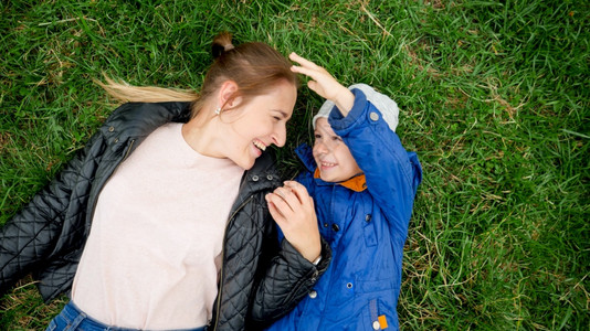 快乐的小男孩肖像年轻母亲躺在草地上玩得开心图片素材