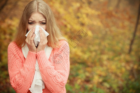 秋天公园的生病妇女打喷嚏在组织上女孩在户外得了感冒鼻炎或过敏卫生保健秋天公园的生病妇女打喷嚏在组织上图片