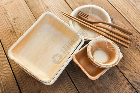具有碗盘杯和木叉勺的一次餐具来自棕榈叶或贝果的生态友好型一次餐具零废物环境概念图片