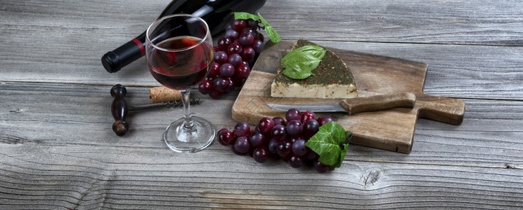 一杯红葡萄酒配有新鲜奶酪加面包叶和生木制餐桌上的葡萄图片
