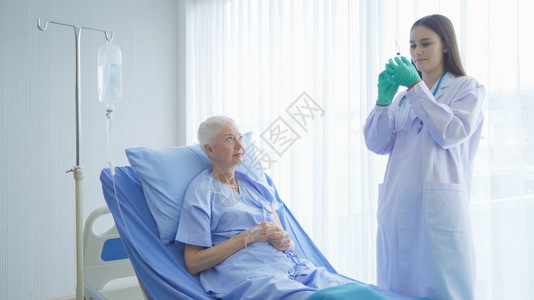 快乐的女医生为病老年女病人提供注射针头疫苗她们躺在医院病房的床上接受医疗和治图片