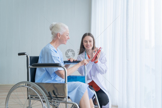 快乐的女医生在疗和保健治概念下在医院病房与轮椅的老年残疾女病人交谈图片