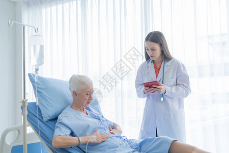 快乐的女医生在疗技术和治概念下对病态的老年女病人说话并使用平板躺在医院病房的床上图片