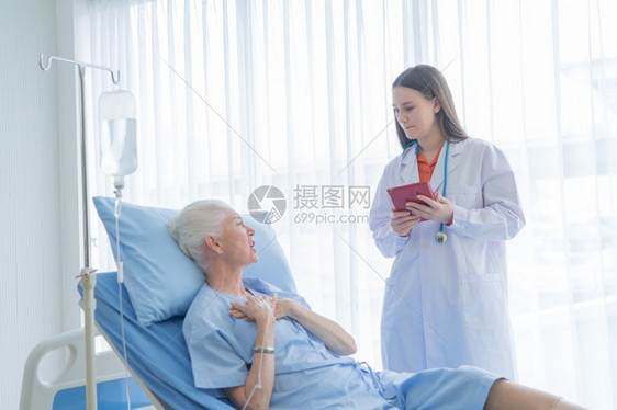 快乐的女医生在疗技术和治概念下对病态的老年女病人说话并使用平板躺在医院病房的床上图片