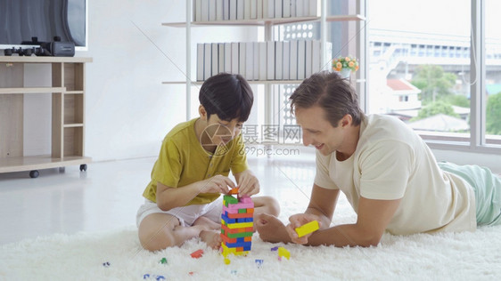 父亲和儿子玩拼图游戏具在家庭活动概念下在家中客厅一起建造多彩的街区塔高加索人父亲和孩子男玩得开心生活方式图片